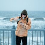 Молодой человек наливает чай из термоса на зимней террасе у моря